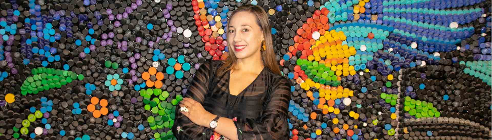 Diana Sabine en la Universidad Ean al frente del mural de tapas plásticas 'Súbete a una movilidad sostenible'